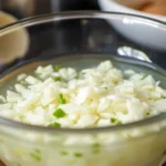 Close-up of minced garlic in water being stirred in a glass bowl, highlighting freshness and